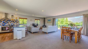 A spacious living area with a kitchen, a dining table, and a sofa. - Terrific views on Totara (Wānaka)