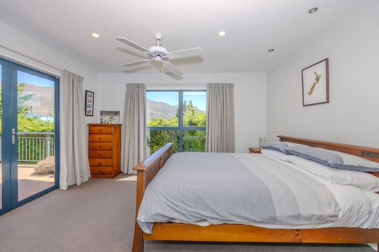 A bedroom with a bed, a ceiling fan, a dresser, and a window with a view of greenery and mountains.