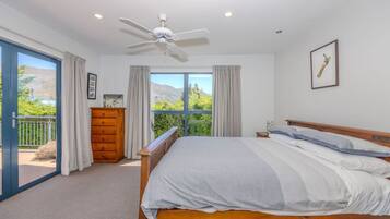 A bedroom with a bed, a ceiling fan, a dresser, and a window with a view of greenery and mountains.