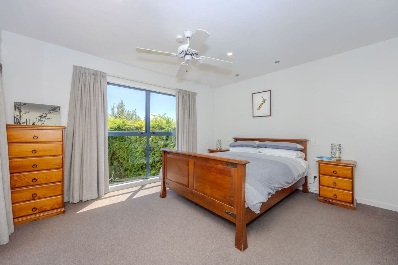 Een slaapkamer met een houten bed, nachtkastje, dressoir, plafondventilator en een raam met gordijnen.