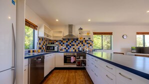 A modern kitchen with white cabinets, a stainless steel dishwasher, a checkered backsplash, and wooden flooring. - Terrific views on Totara (Wānaka)
