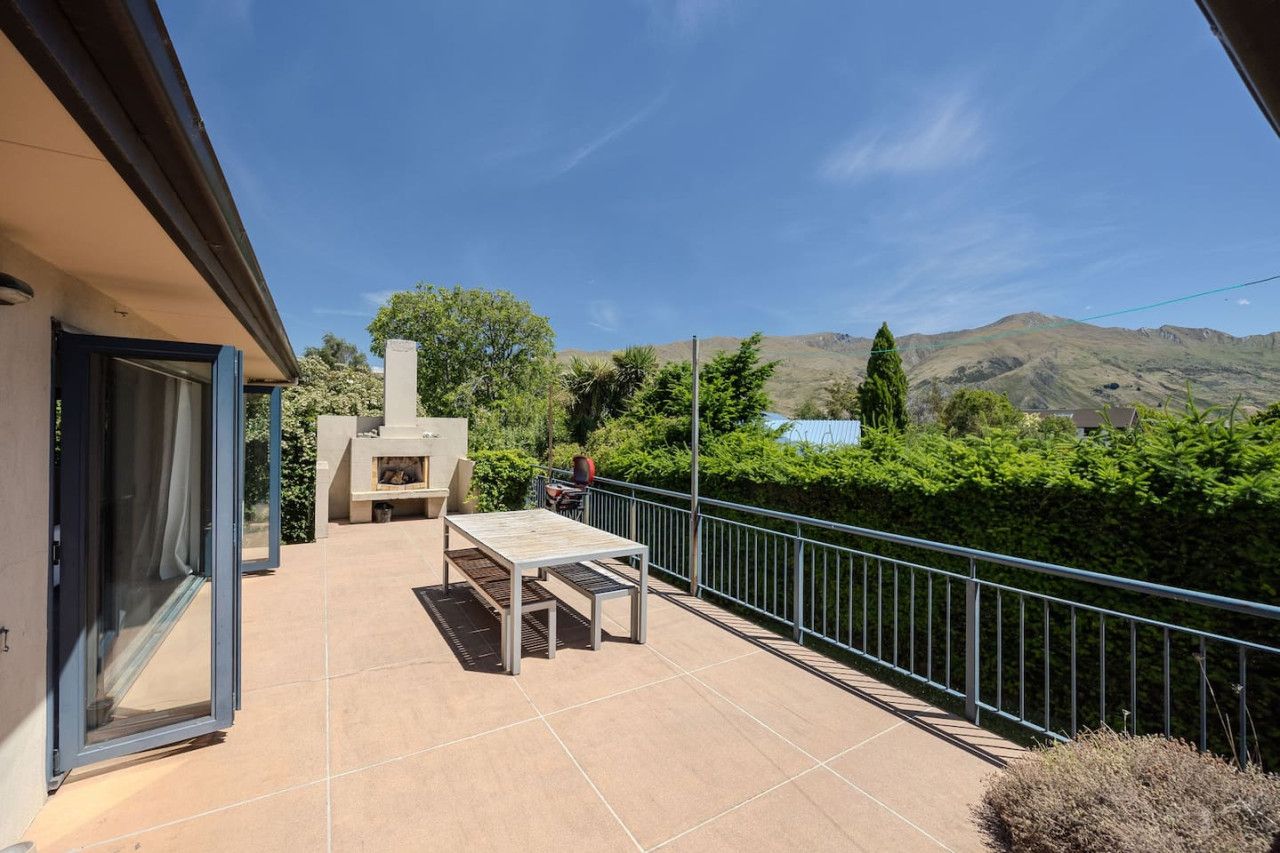 An outdoor patio with a table and chairs, a barbecue grill, and a view of mountains.