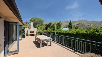 An outdoor patio with a table and chairs, a barbecue grill, and a view of mountains.