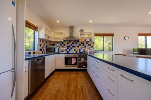 A modern kitchen with white cabinets, a stainless steel dishwasher, a microwave, and a stove. - Terrific views on Totara (Wānaka)