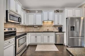 Cozinha moderna com armários brancos, eletrodomésticos de aço inoxidável e painel de azulejos.