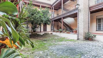 A courtyard with a cobblestone floor, potted plants, and a staircase leading to an upper level.
