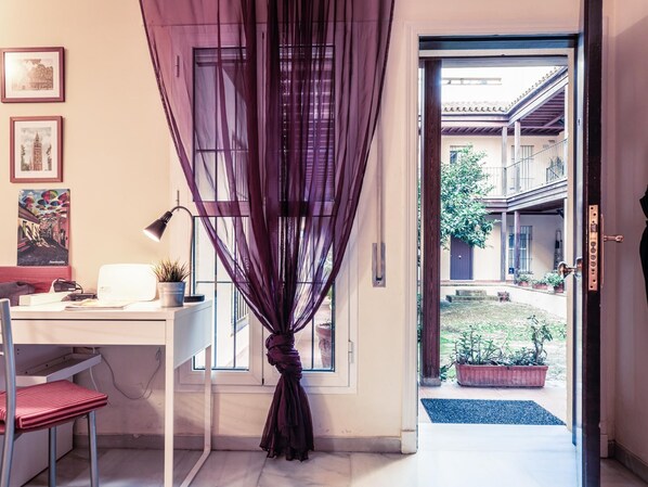 A room with a desk, chair, and a view of a courtyard with potted plants and a building in the background. - Sevilla Best Location Triana Apartment (Sevilla)
