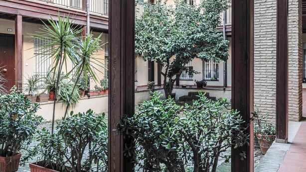 Une cour agrémentée de plantes en pot, une pergola en bois et un bâtiment doté de balcons.