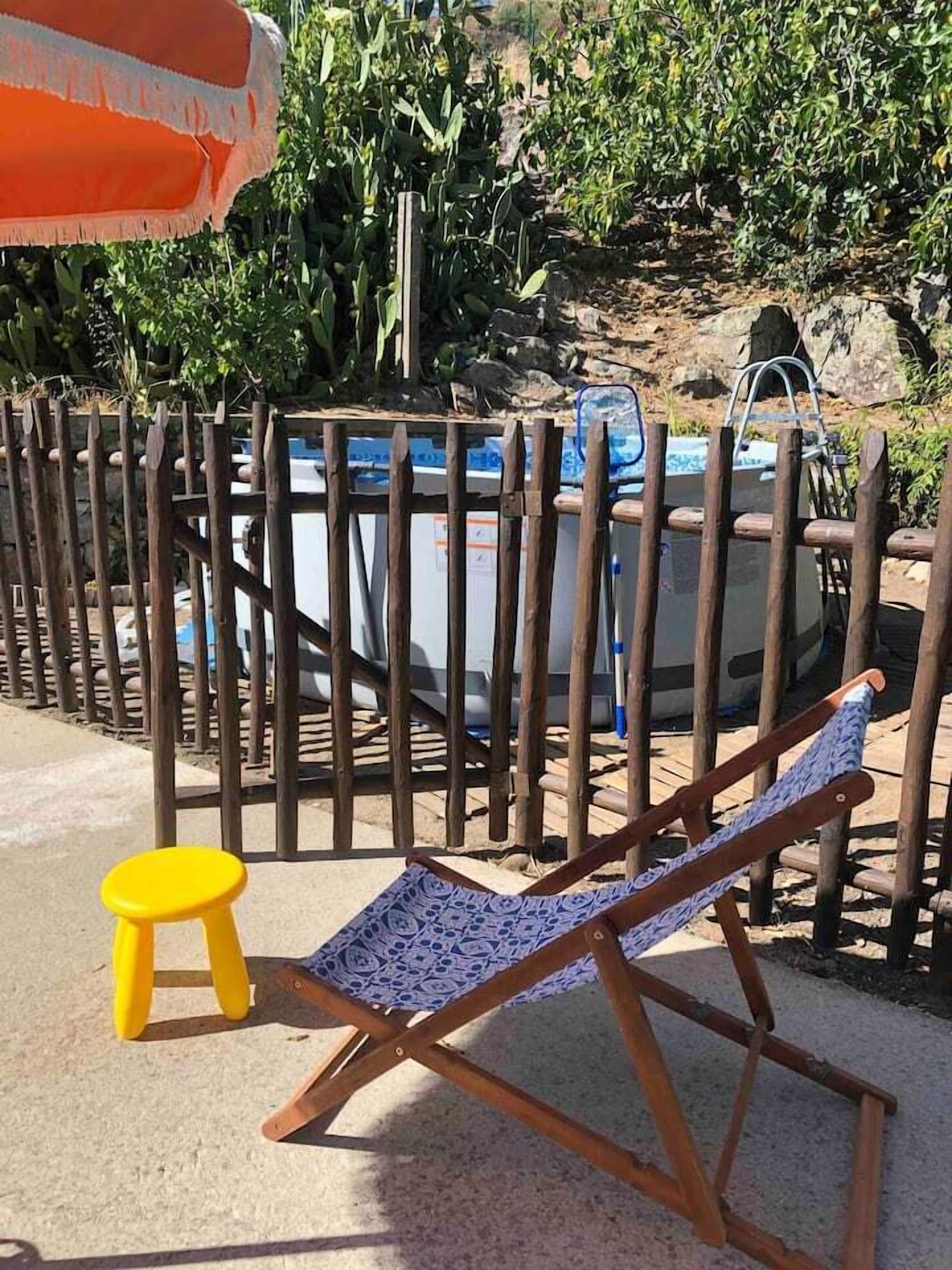 Una valla de madera, una piscina y un taburete amarillo.
