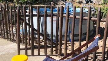 Una valla de madera, una piscina y un taburete amarillo.