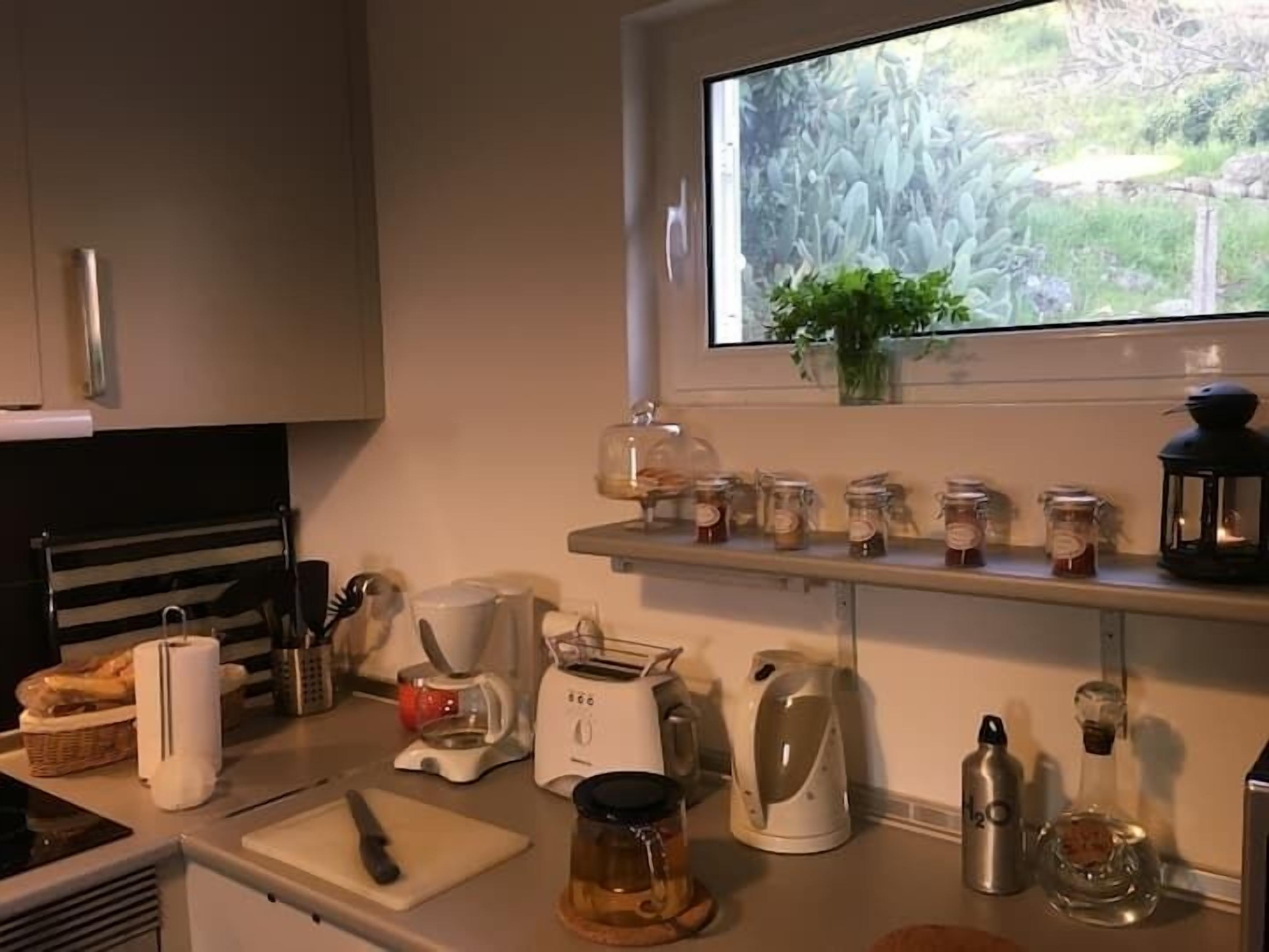 Een keuken met een raam, een broodrooster, een waterkoker en diverse potjes op het aanrecht.