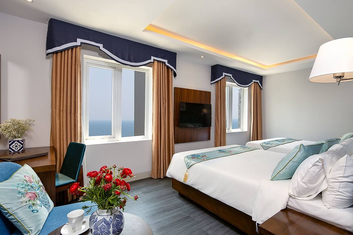 A hotel room with two beds, a TV, a desk with a chair, and a window with curtains.