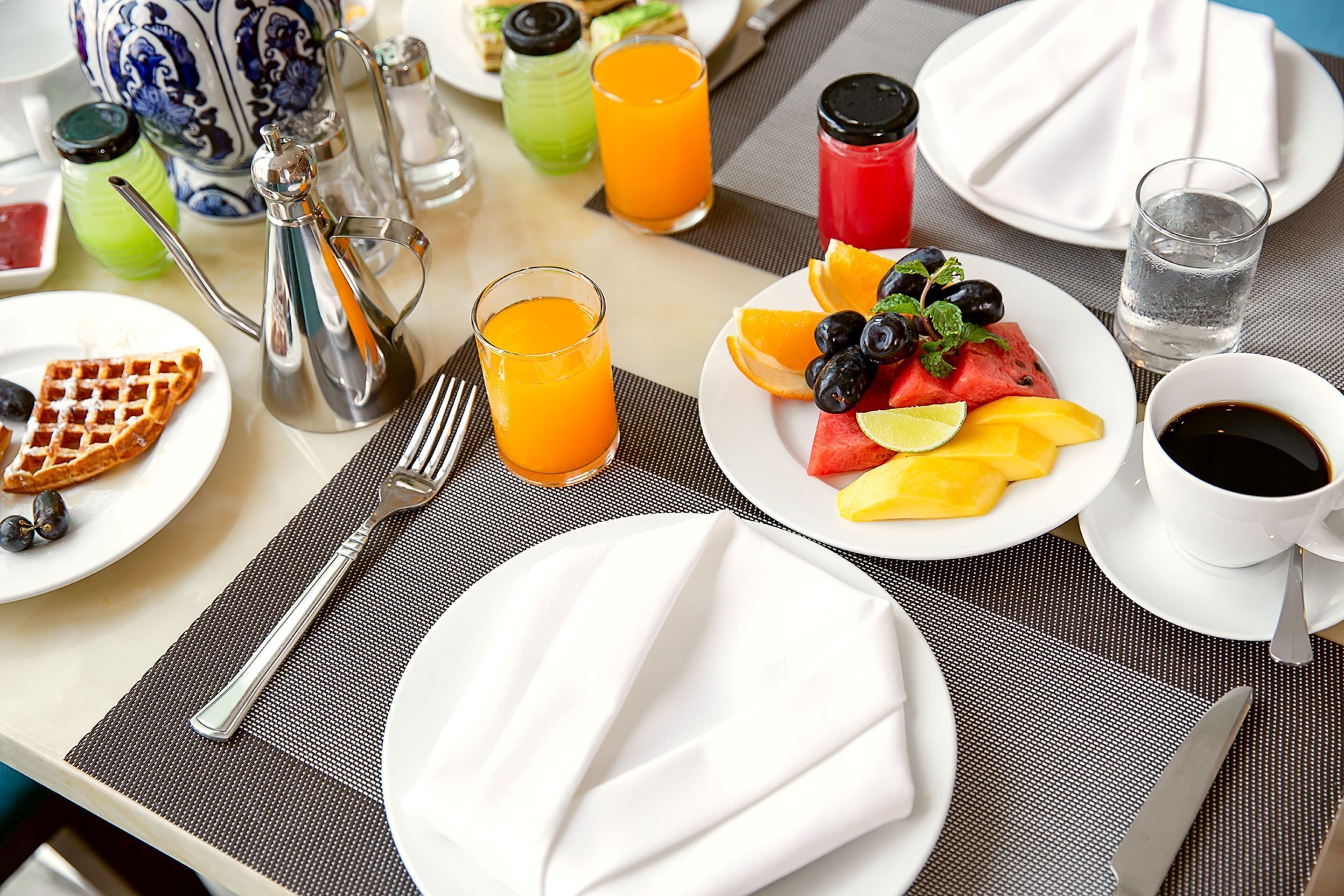 A breakfast setting with waffles, fruit, coffee, and juice.