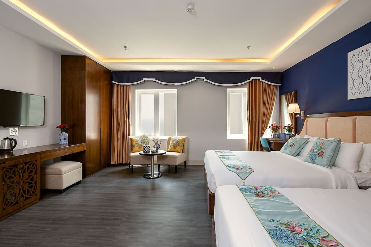A hotel room with a large bed, a desk with a TV, a small table with a vase of flowers, and a sofa.