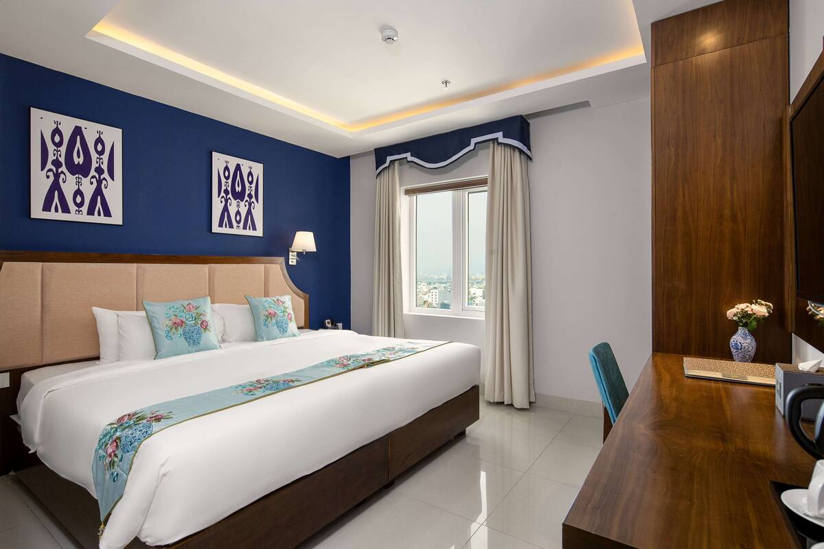 A modern hotel room with a large bed, a wooden desk, and a city view.