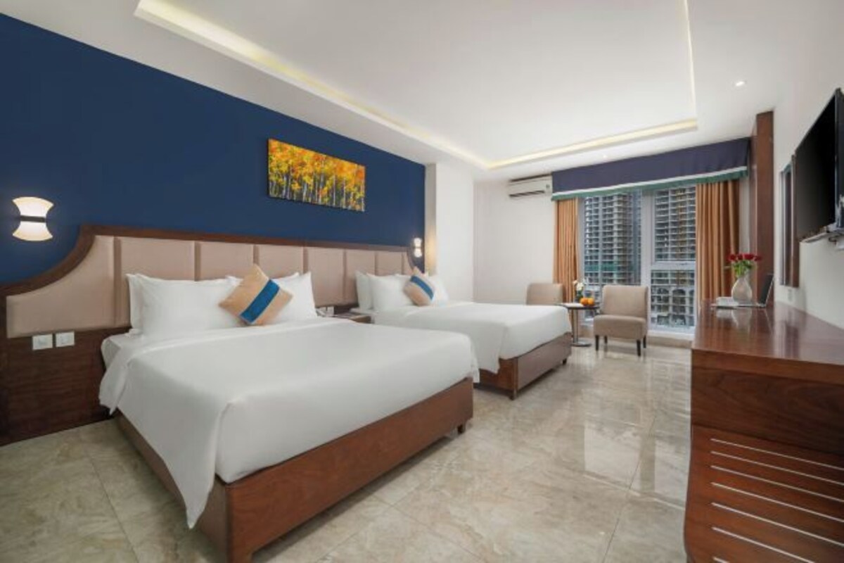 A hotel room with two beds, a desk, a chair, and a TV.