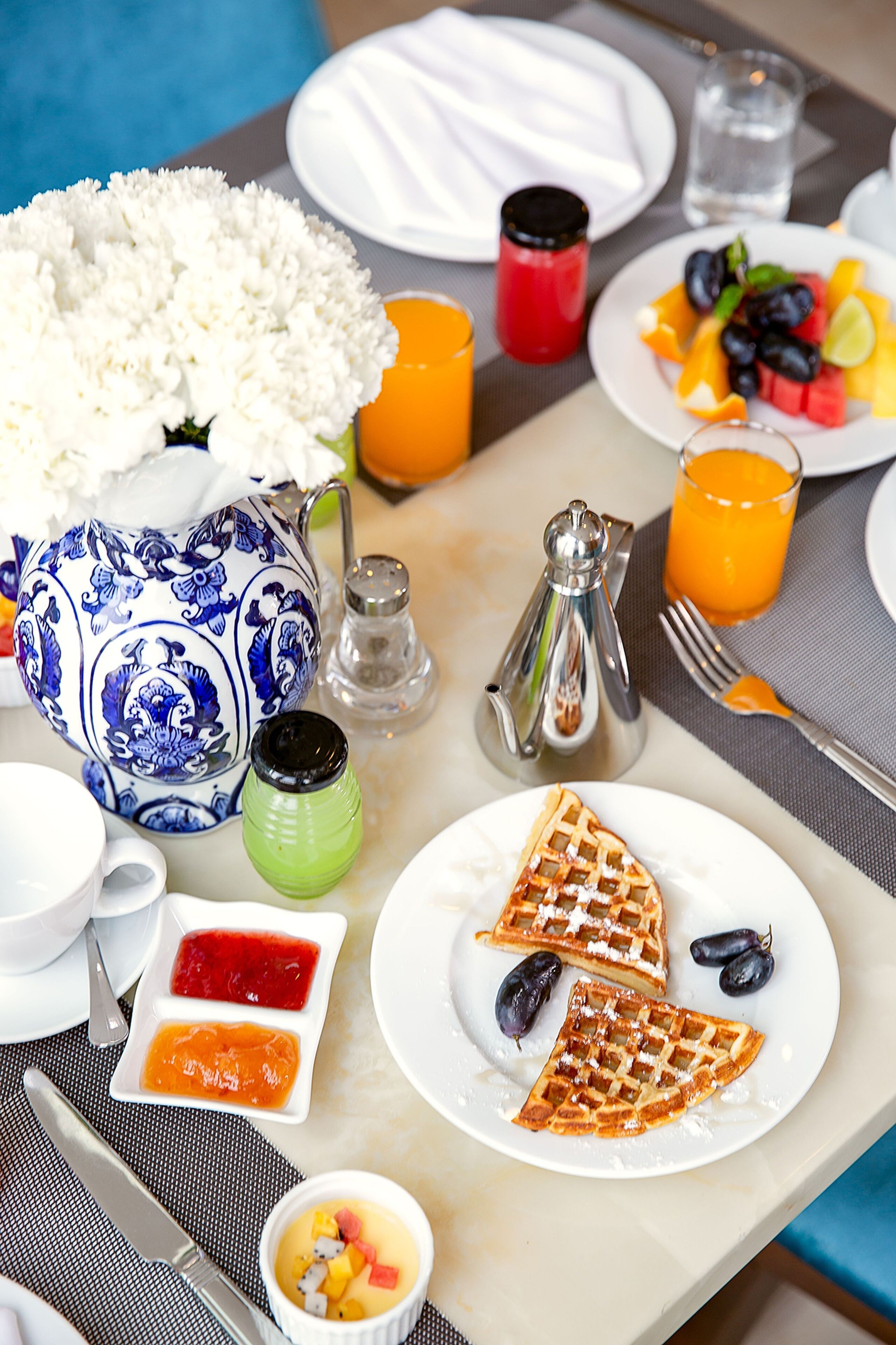 Een ontbijttafel met een karaf, zout- en peperstel, een wafelbord, fruit en een bloevas.