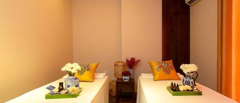 Habitación de hotel con dos camas, cada una con cubrecama y almohadas amarillas a juego. Hay jarrones decorativos con flores sobre las camas, una mesita con una bandeja de objetos y un equipo de aire acondicionado en la pared.