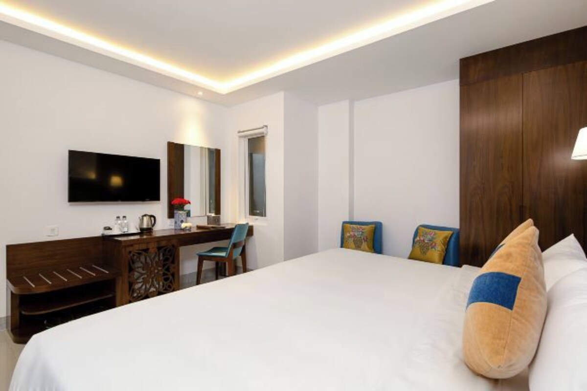A hotel room with a large bed, a desk with a chair, a flat-screen TV, and a wooden wardrobe.