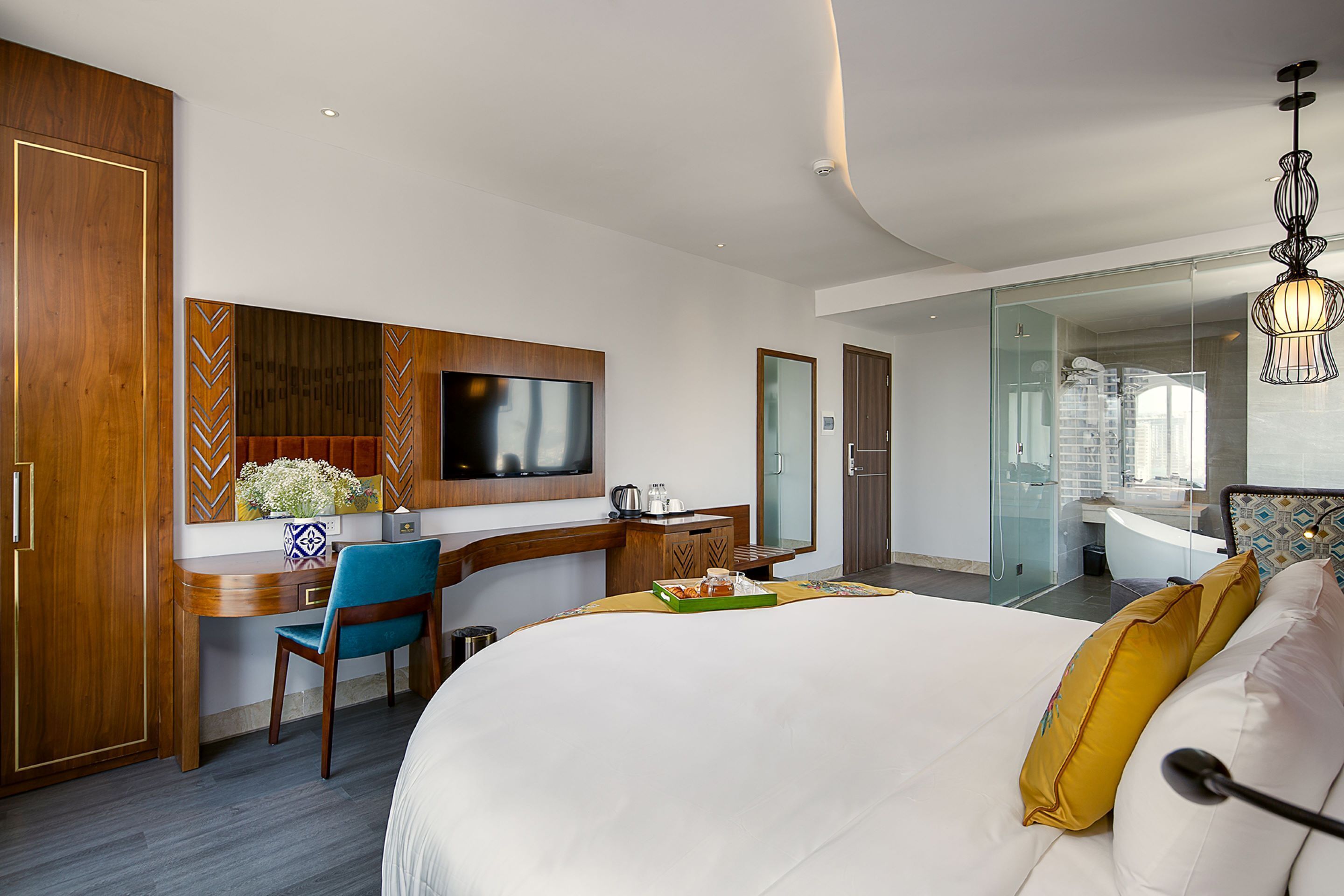 Une chambre d’hôtel avec un grand lit, un bureau avec une chaise, une télévision et une salle de bain visible à travers une porte en verre.