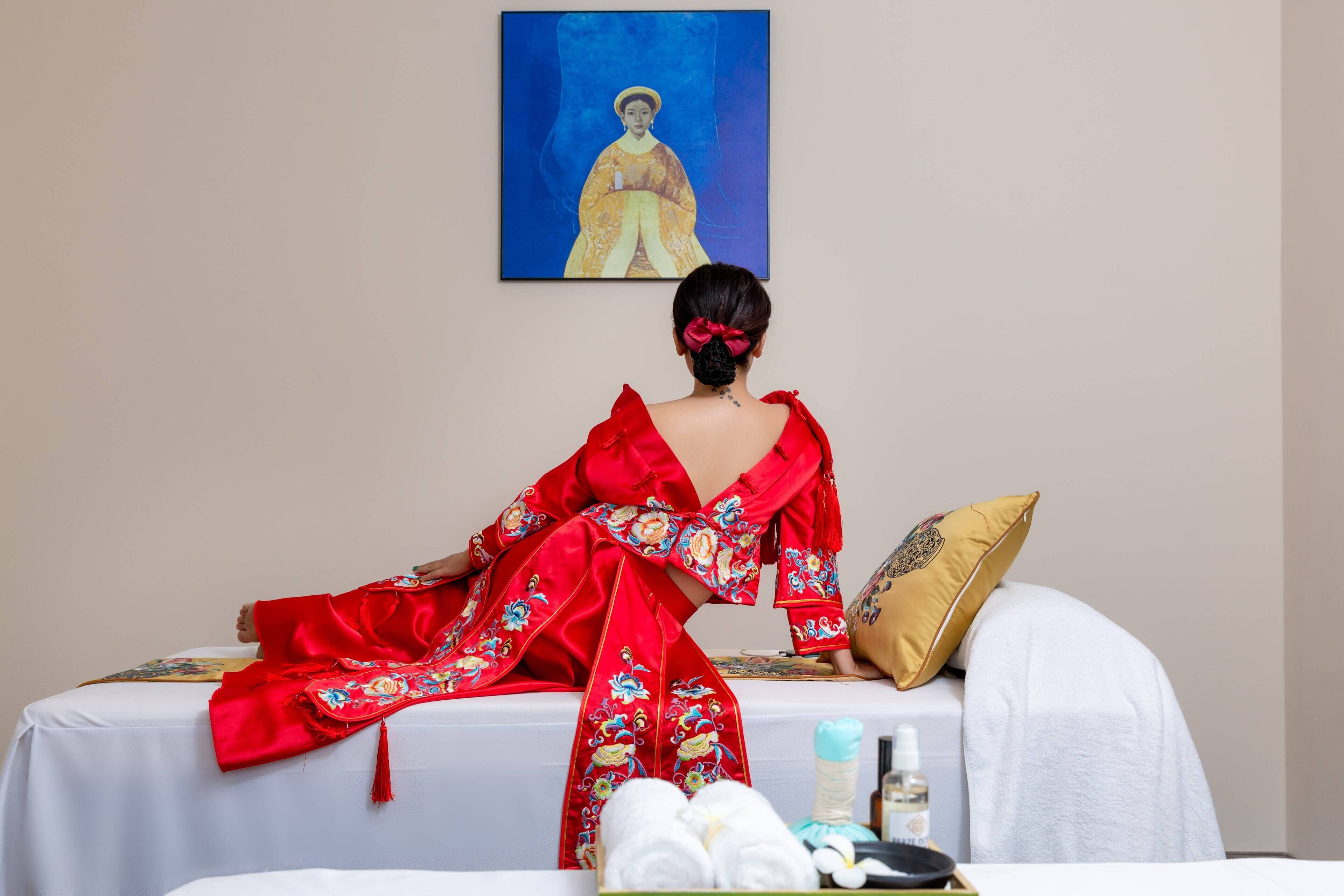 A room with a bed, a painting on the wall, and a person in a red robe.