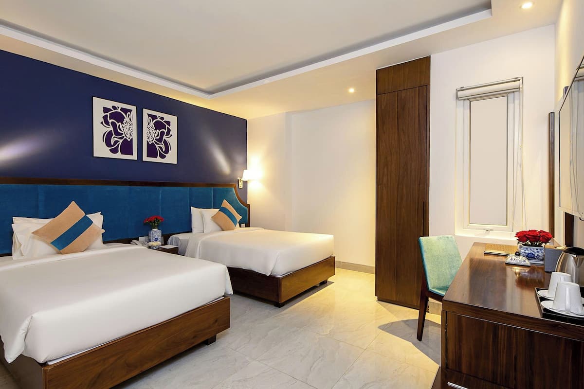 A hotel room with two beds, a desk, a chair, and a large mirror.