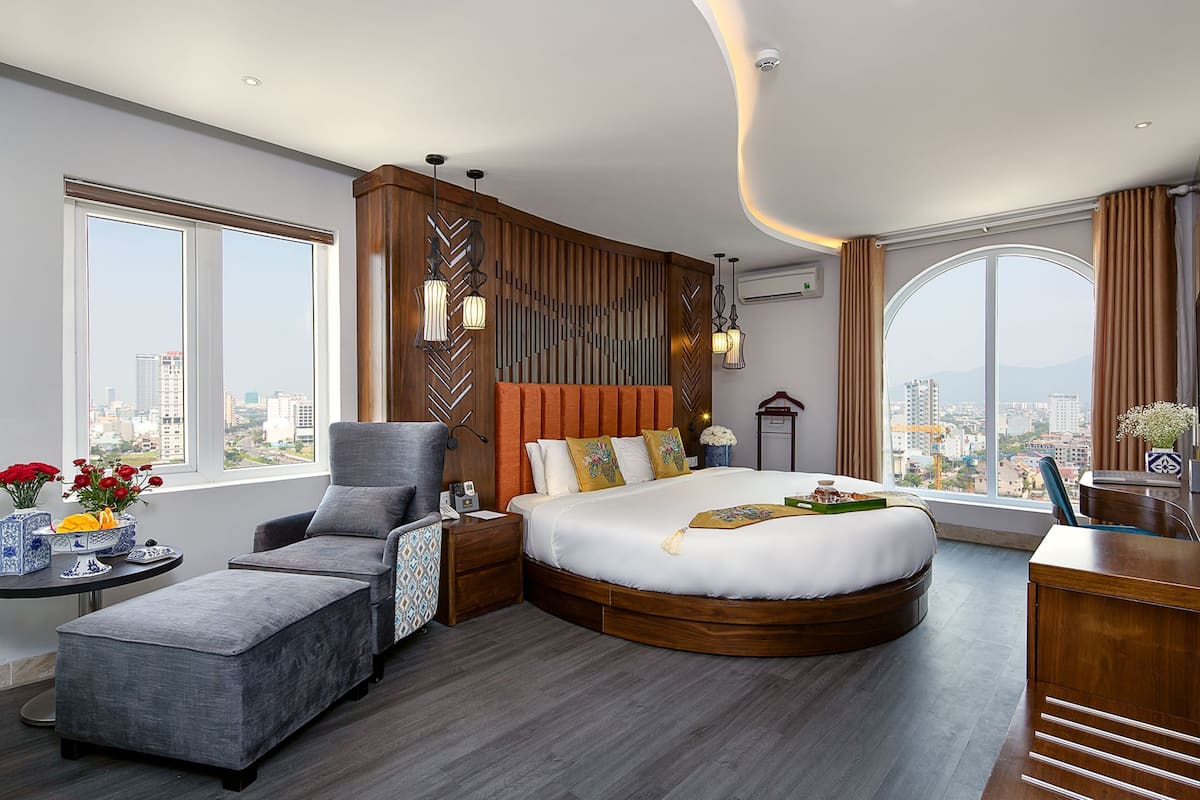A modern hotel room with a large bed, a seating area, and a view of the city.