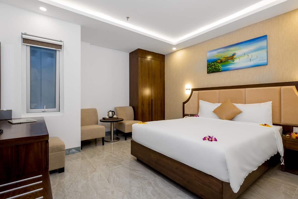 A hotel room with a large bed, a desk, a chair, a small table, and a painting on the wall.