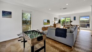 Amplia sala de estar con mesa de fútbol, un sofá gris y una zona de comedor con mesa y sillas.