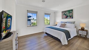 Un dormitorio con una cama, dos ventanas, un cuadro, una lámpara y un televisor.