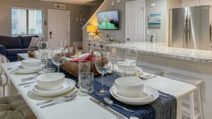 Una cocina moderna con comedor listo para una comida, que incluye una isla grande, electrodomésticos de acero inoxidable y un televisor montado en la pared.