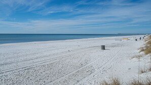 Una playa nevada con cielo despejado y un muelle distante.