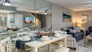 Un comedor con una mesa larga dispuesta para una comida, un sofá y un televisor al fondo.