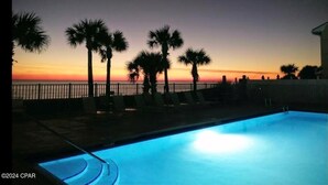 Una piscina con vista al atardecer, palmeras y una valla.