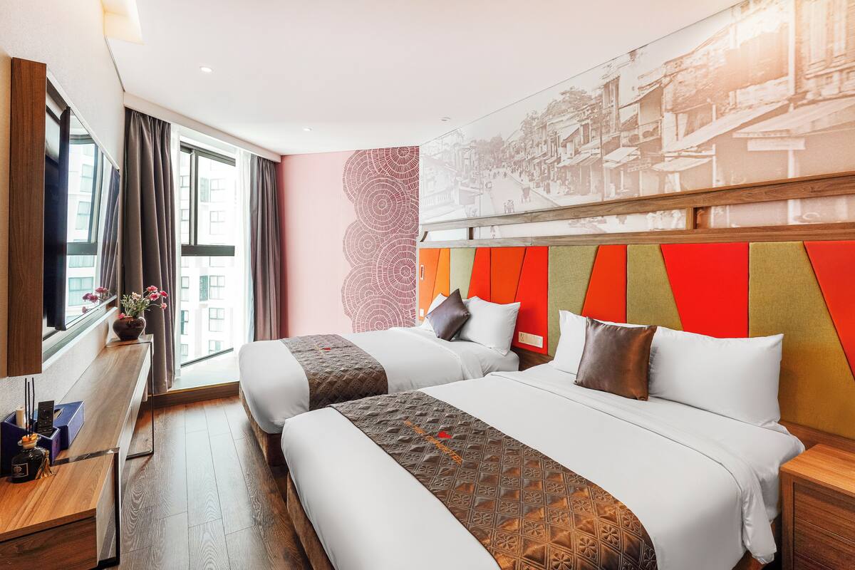 A hotel room with two beds, a wooden desk, and a large window.