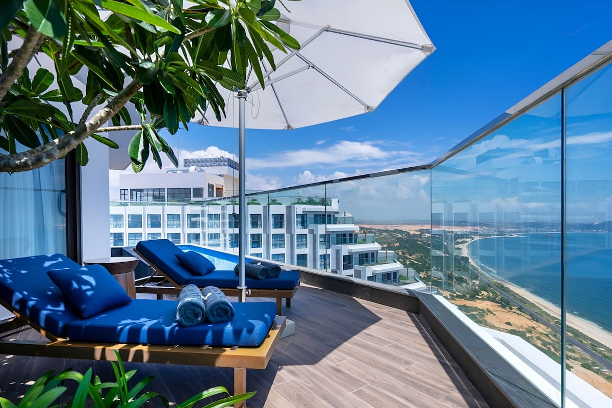 A rooftop lounge with blue cushioned chairs and a large umbrella, overlooking a coastal cityscape.