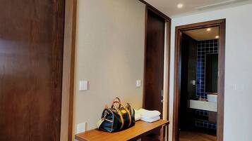 Habitación de hotel con un escritorio de madera, una silla roja, un espejo grande y un baño visible a través de una puerta abierta.
