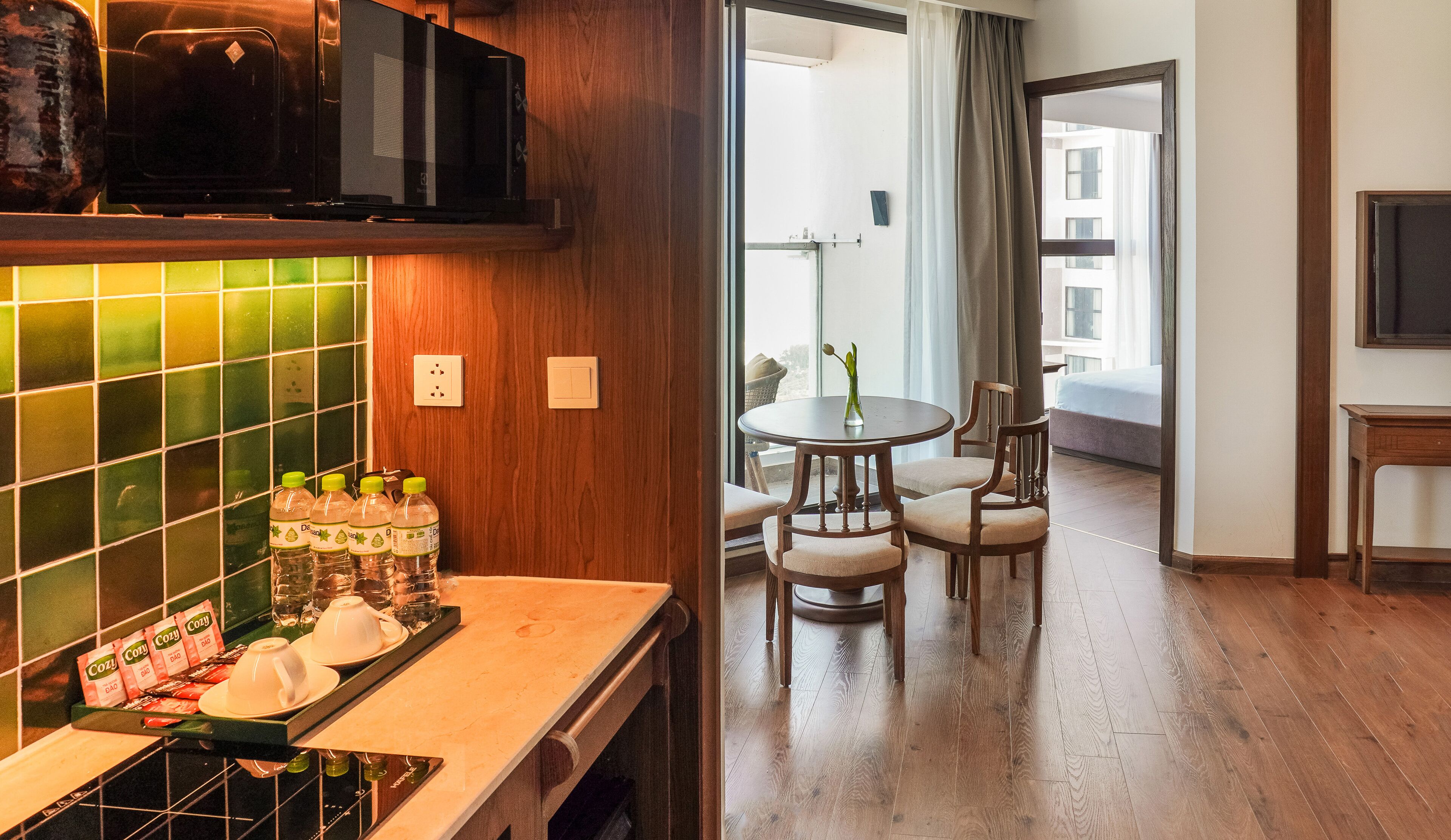 Una cocina equipada con microondas, cafetera y un salpicadero de azulejos. Hay una zona de comedor con mesa y sillas, y una vista al exterior a través de una ventana.