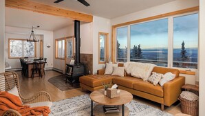 A spacious living room with a large window, a fireplace, and a dining area. - Norrsken View - Sauna - Mountains - Deck - Aurora - Family Friendly - Wifi (Fairbanks)