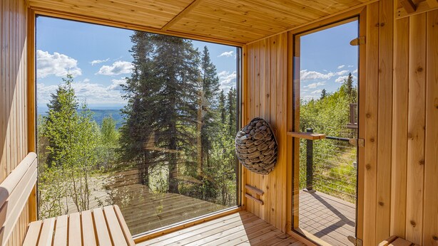 A wooden deck with a bench, a large window, and a view of a forest and lake. - Norrsken View - Sauna - Mountains - Deck - Aurora - Family Friendly - Wifi (Fairbanks)