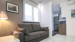 Ein modernes Wohnzimmer mit einem grauen Sofa, einer Blumenvase, einer Lampe und einem gerahmten Bild an der Wand.