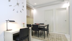 Ein moderner Essbereich mit einem weißen Tisch, schwarzen Stühlen, einer Wanduhr und einem kleinen Schreibtisch mit einer Lampe.