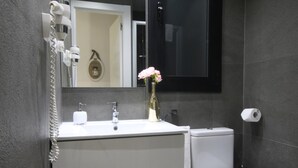 Une salle de bain moderne avec un lavabo blanc, un vase doré orné de fleurs, un miroir et des toilettes.
