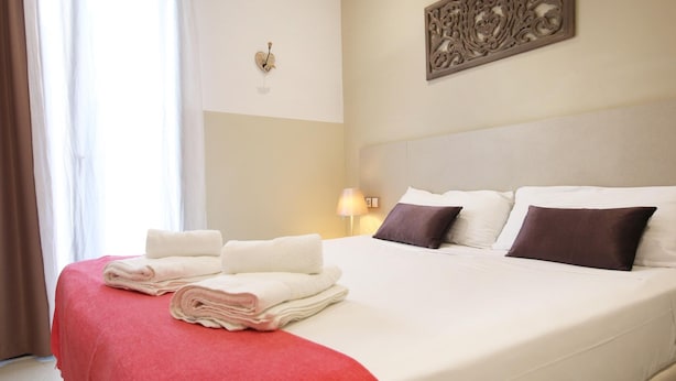 Una habitación de hotel con una cama bien hecha, una manta roja y un adorno en la pared.