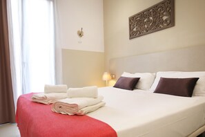 Ein Hotelzimmer mit einem ordentlich bezogenem Bett, einer roten Tagesdecke und einem an der Wand befestigten dekorativen Gegenstand.