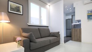 Una sala de estar moderna con un sofá gris, una mesita con un florero, una lámpara y una fotografía de un paisaje urbano en la pared.