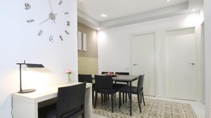 Un comedor moderno con una mesa blanca, sillas negras, un reloj y un escritorio con una lámpara.