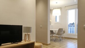 Un salon moderne avec un téléviseur à écran plat, une lampe et un pouf en osier.