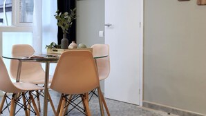 Un coin repas avec une table en verre et quatre chaises, un vase avec des plantes et un panneau fixé au mur sur lequel on peut lire « DÉFENSE DE FUMER ».