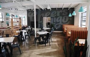 A modern cafe with black chairs, white tables, and a large 'Cheers Hugo' mural. - The Scissortail, a Wheeler District Downtown Stay (Oklahoma City)